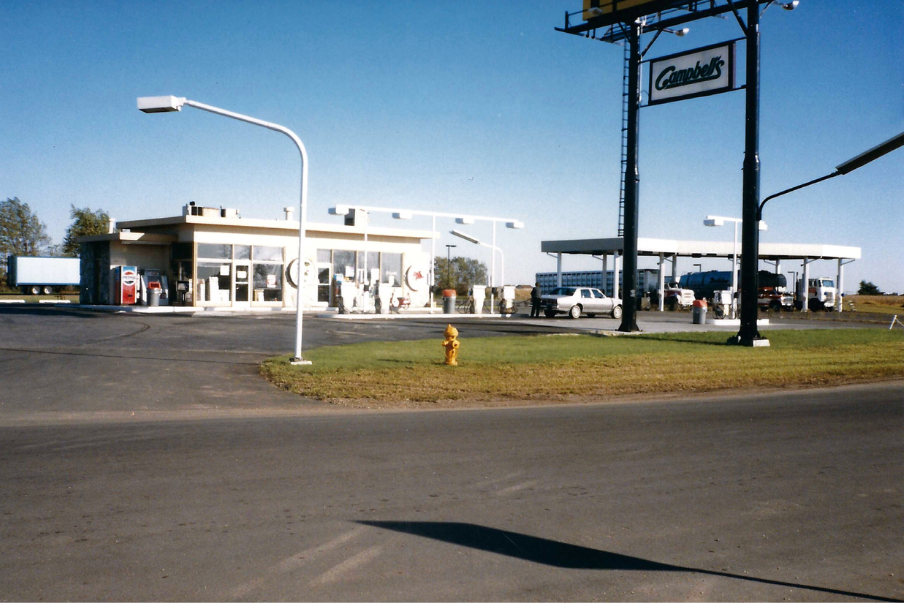 Gas station with a sign, pumps, and a small building under a blue sky.