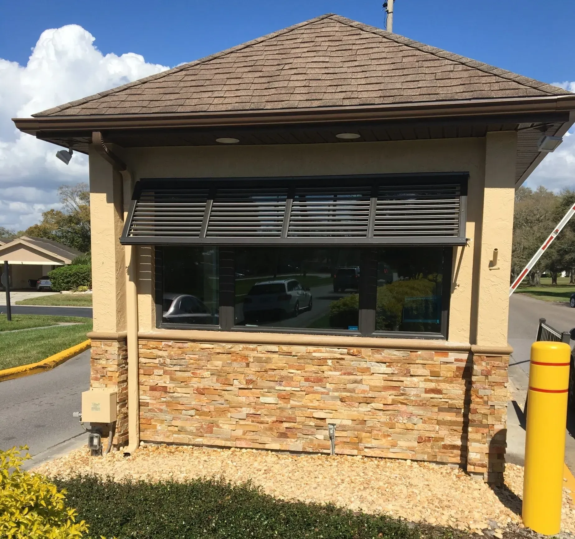 Guardhouse with stone facade, dark window, and tan roof, near a gated entrance.