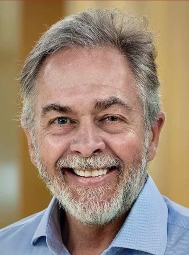 Smiling older man with graying beard and blue shirt.