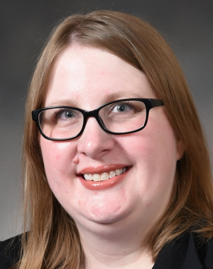 Woman with glasses smiles, blonde hair, neutral background.
