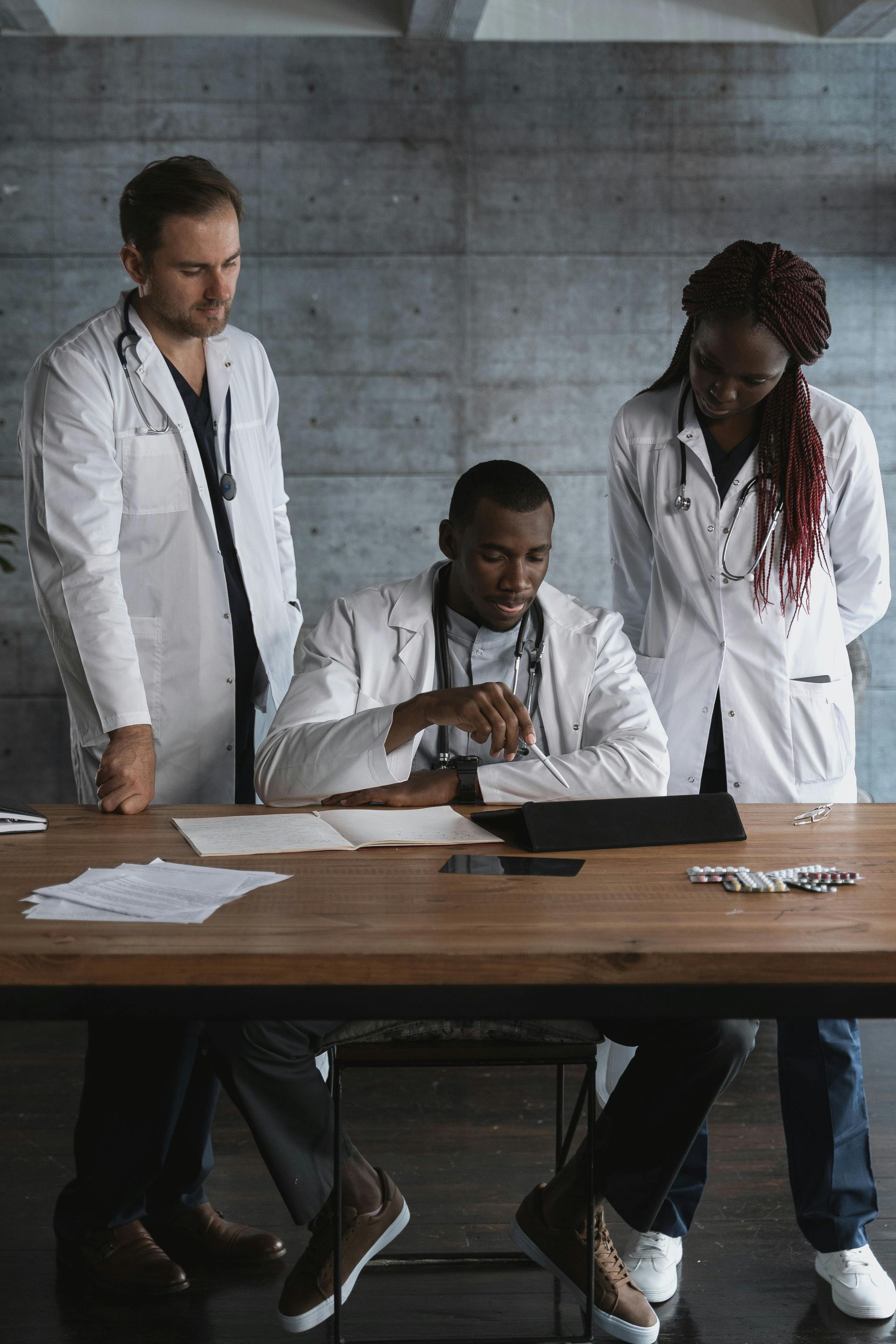 Three doctors in white coats reviewing documents at a table. A somber mood is conveyed.