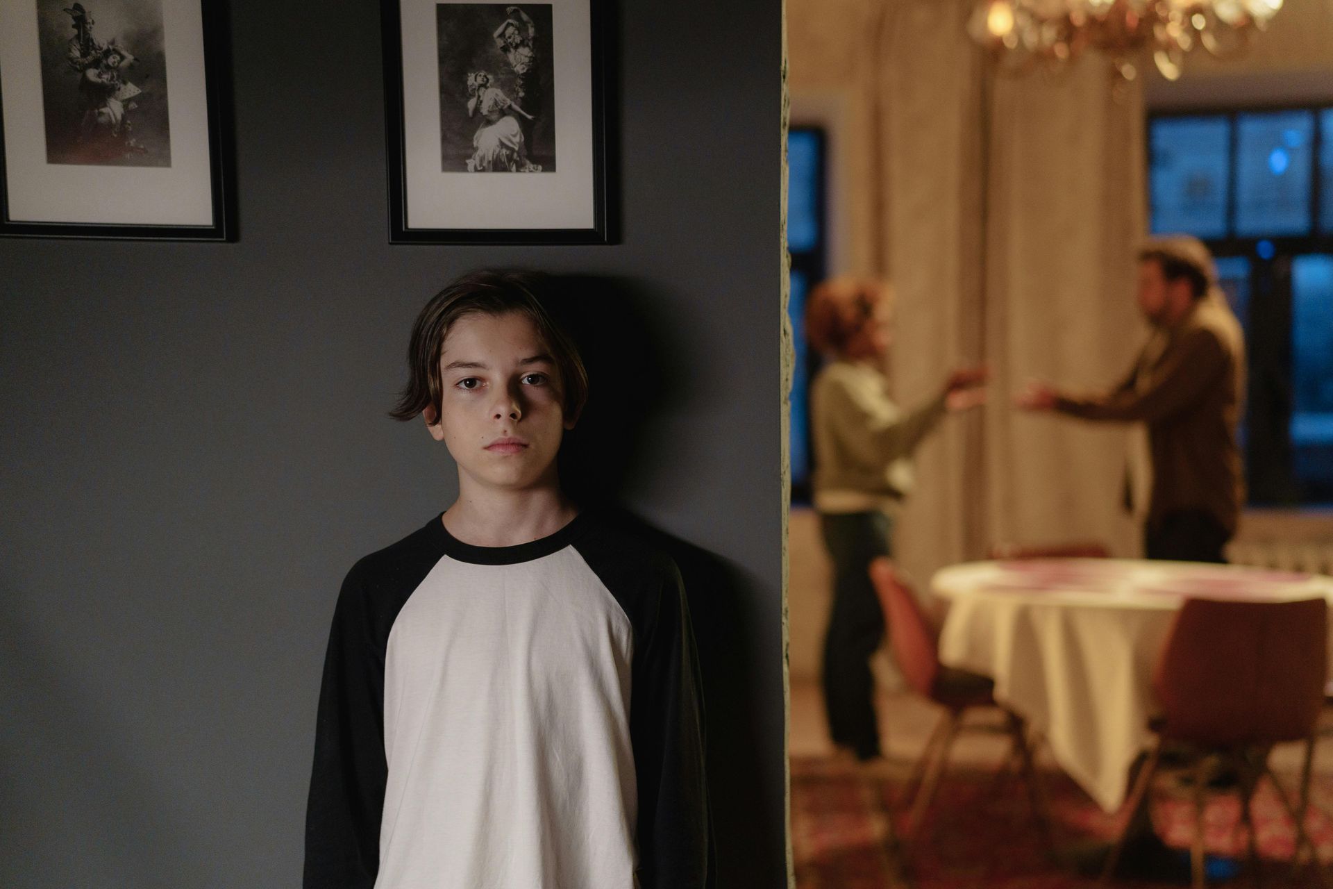 Boy in baseball shirt watches parents argue in the dining room; a tense family moment.