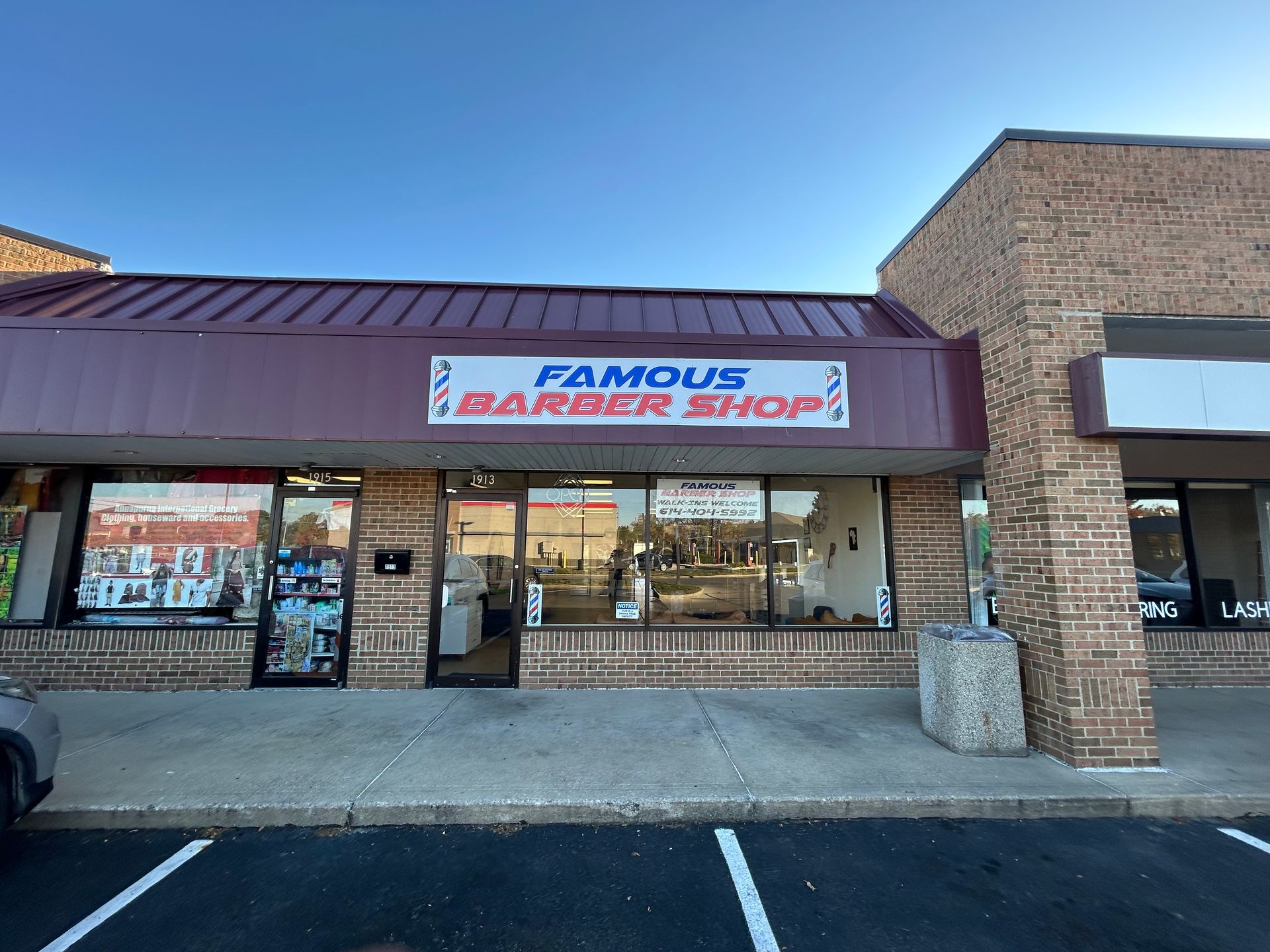 Famous Barber Shop storefront with a red sign and glass windows in a brick plaza.