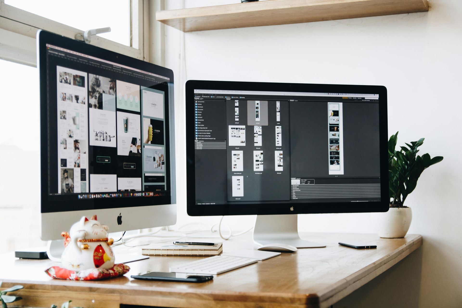 Design workspace with dual monitors and a desk plant.