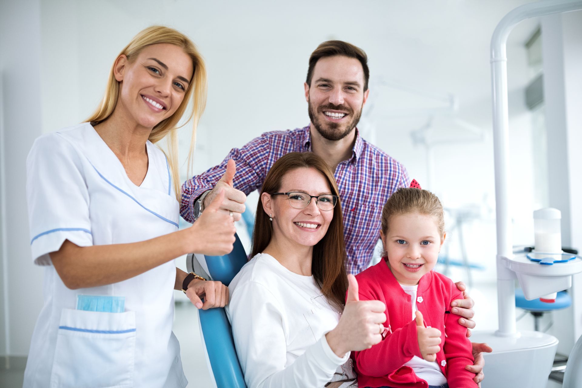 Dental professional, two adults, and a child giving thumbs up in a dental clinic. Dental professional, two adults, and a child giving thumbs up in a dental clinic.