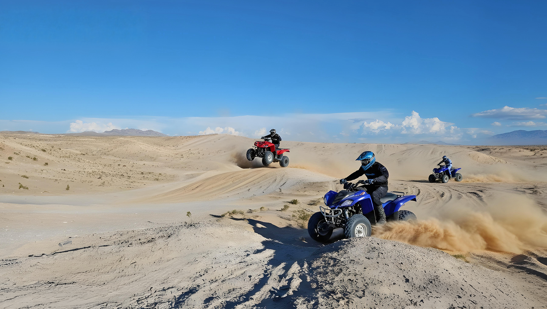 Three people riding all-terrain vehicles through a sandy desert landscape under a clear blue sky.