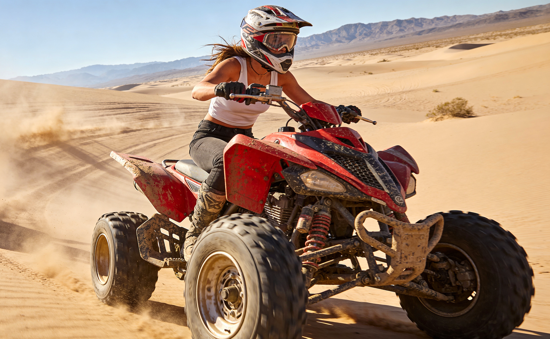 A person wearing a helmet riding a red ATV through a sandy desert landscape.