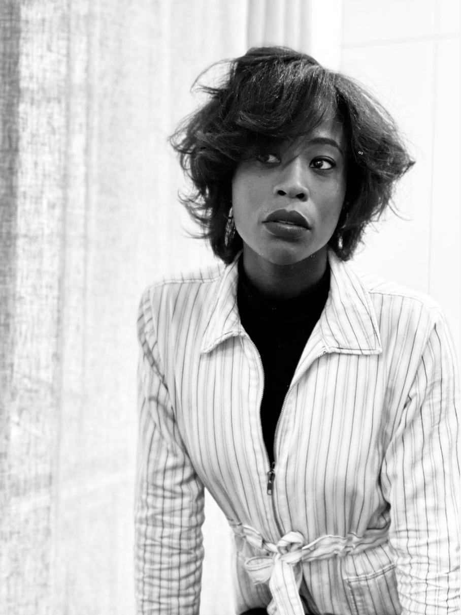 Femme en veste rayée et col roulé noir, regardant hors champ.