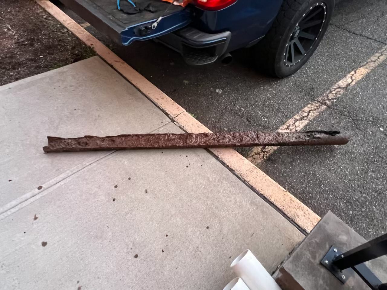 A piece of metal is laying on the sidewalk next to a car