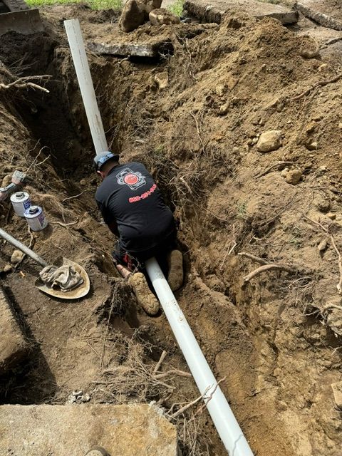 A man is kneeling in the dirt next to a pipe.