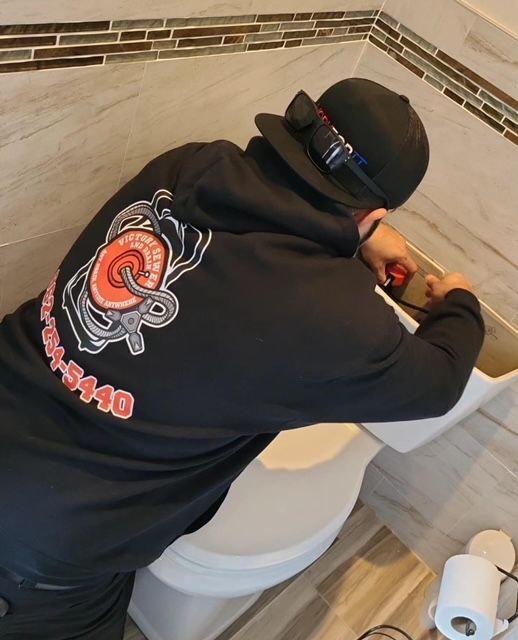A man wearing a hat and a black shirt with the number 5440 on the back is working on a toilet