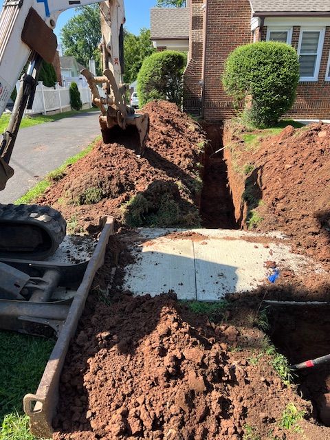 An excavator is digging a trench in front of a house
