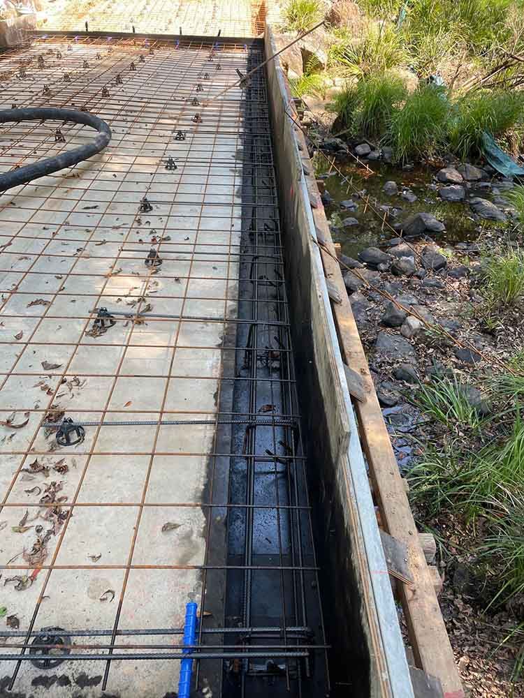 Concrete Wall Is Being Built Next To A Stream — Providing Steel & Concrete Construction In Lismore, NSW