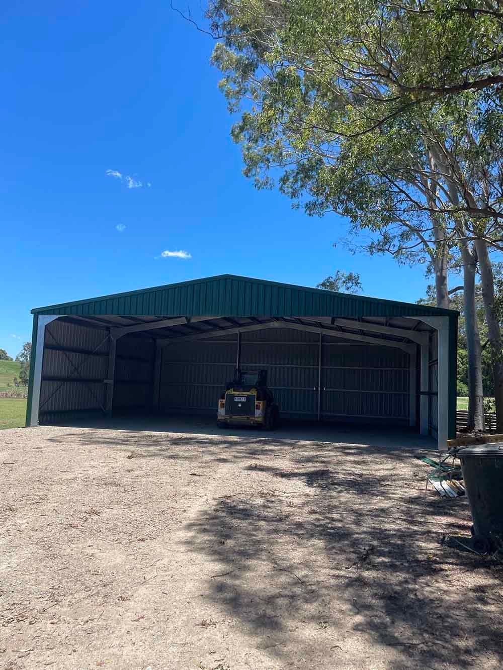 Shed With A Green Roof Is Sitting In The Middle Of A Dirt Road — Providing Steel & Concrete Construction In Gold Coast, QLD
