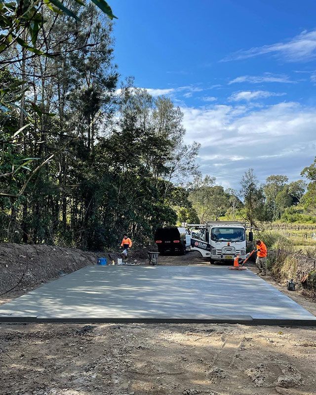 A Concrete Driveway Is Being Built In The Middle Of A Forest With Two Construction Man — CJR Group Concrete Construction In Lismore, NSW