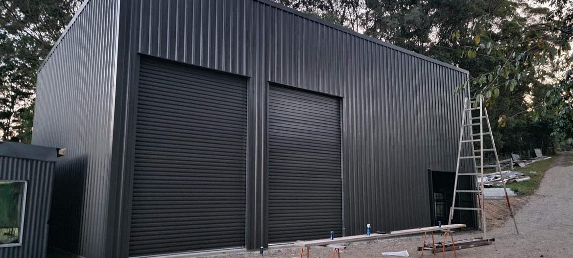 Black Metal Building With A Ladder In Front Of It — Providing Steel & Concrete Construction In Lismore, NSW