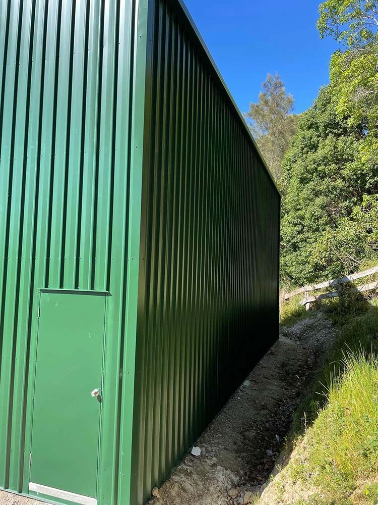 Green Metal Building With a Door on the Side of It — Providing Steel & Concrete Construction in Eviron, NSW