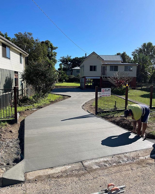 A Man Is Working On A Large Concrete Driveway In Front Of A House  —CJR Group Concrete Construction In Tweed Heads, NSW