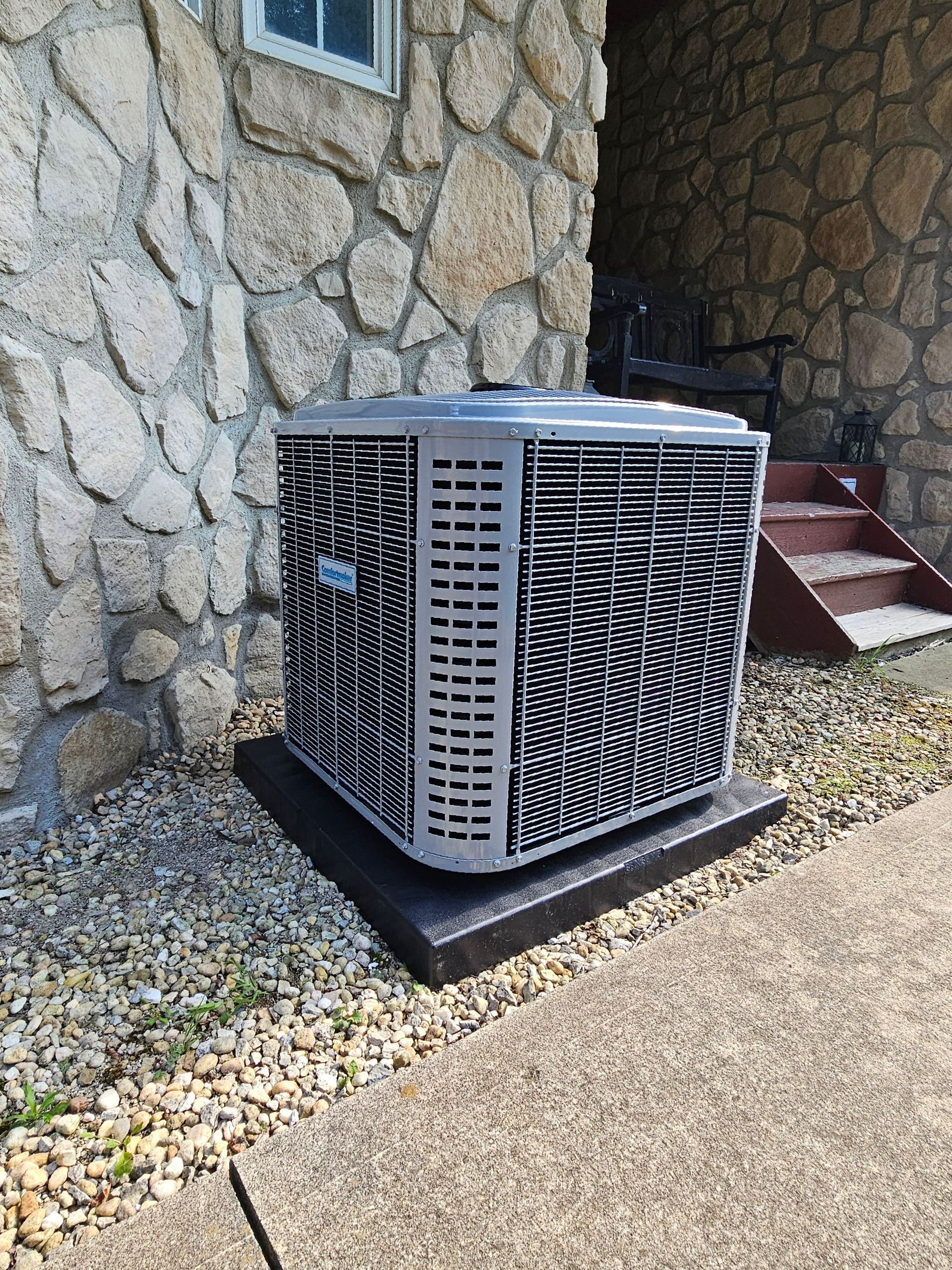 A large air conditioner is sitting on the side of a stone building.
