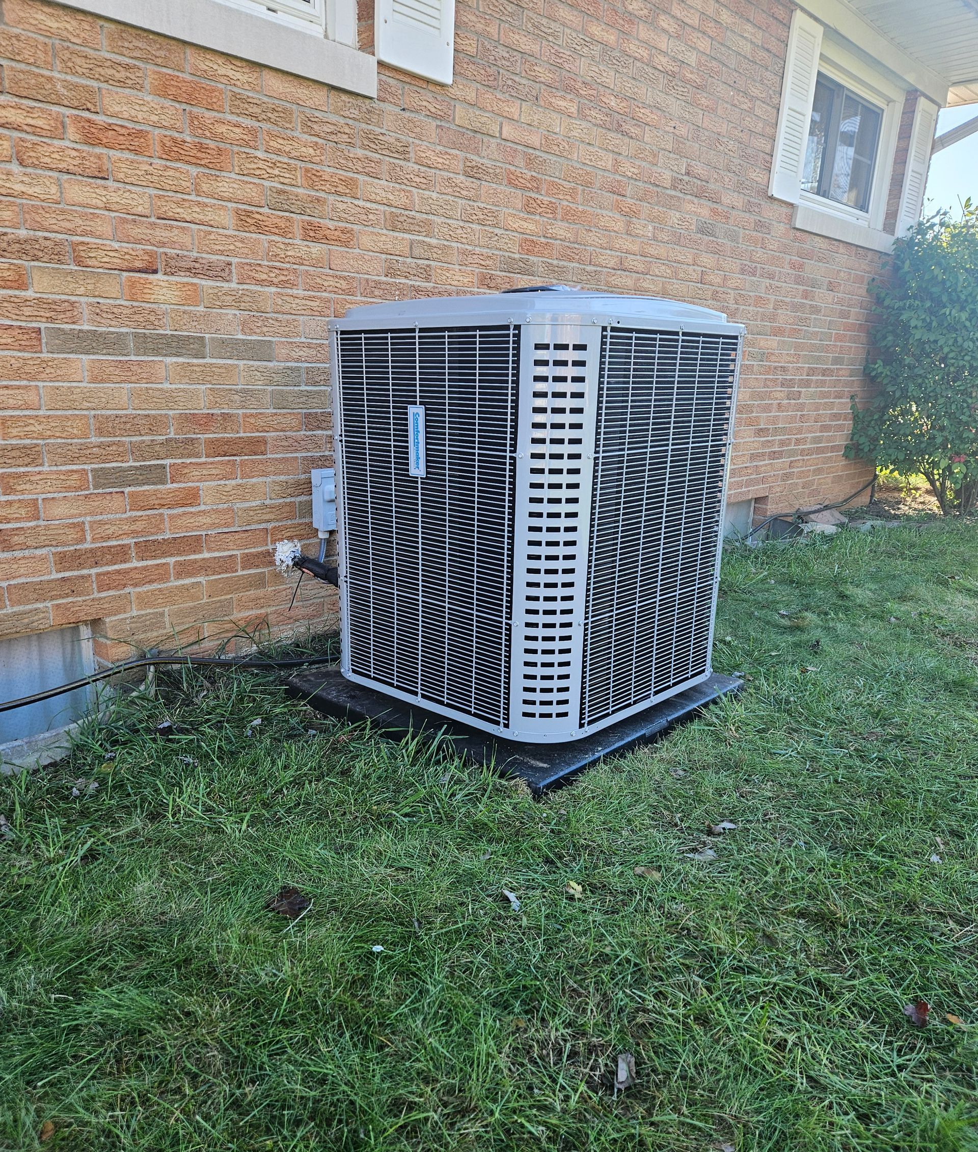 A large air conditioner is sitting in the grass in front of a brick building.