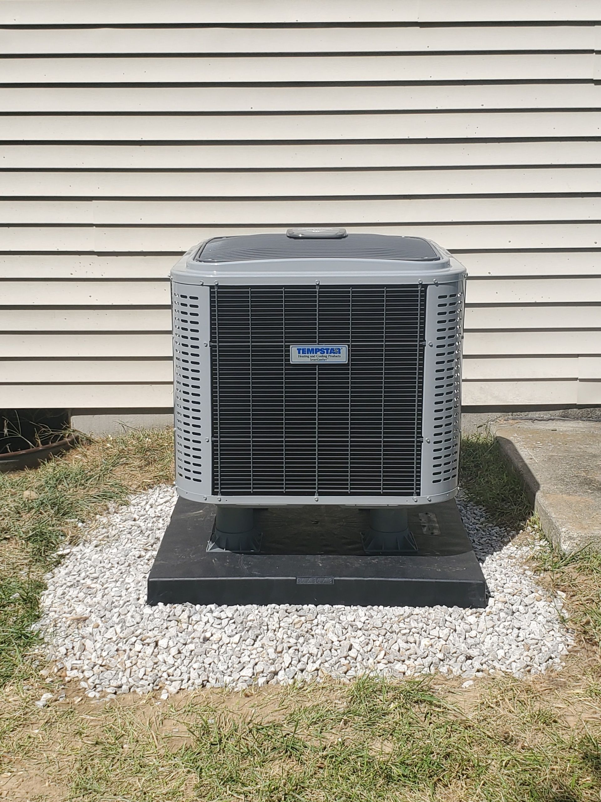 An air conditioner is sitting on top of a pile of gravel in front of a house.