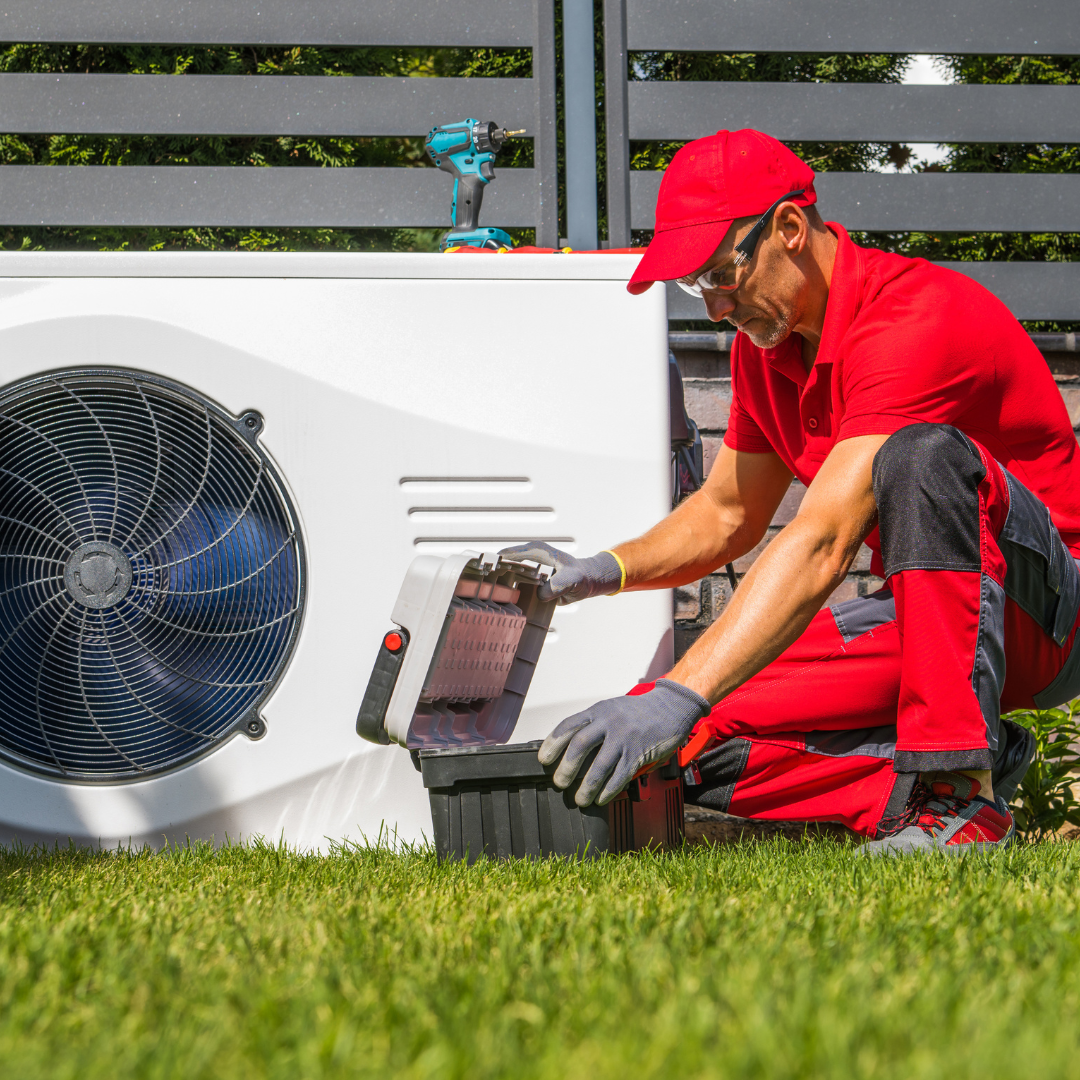 A man in a red shirt and black pants is working on an air conditioner.