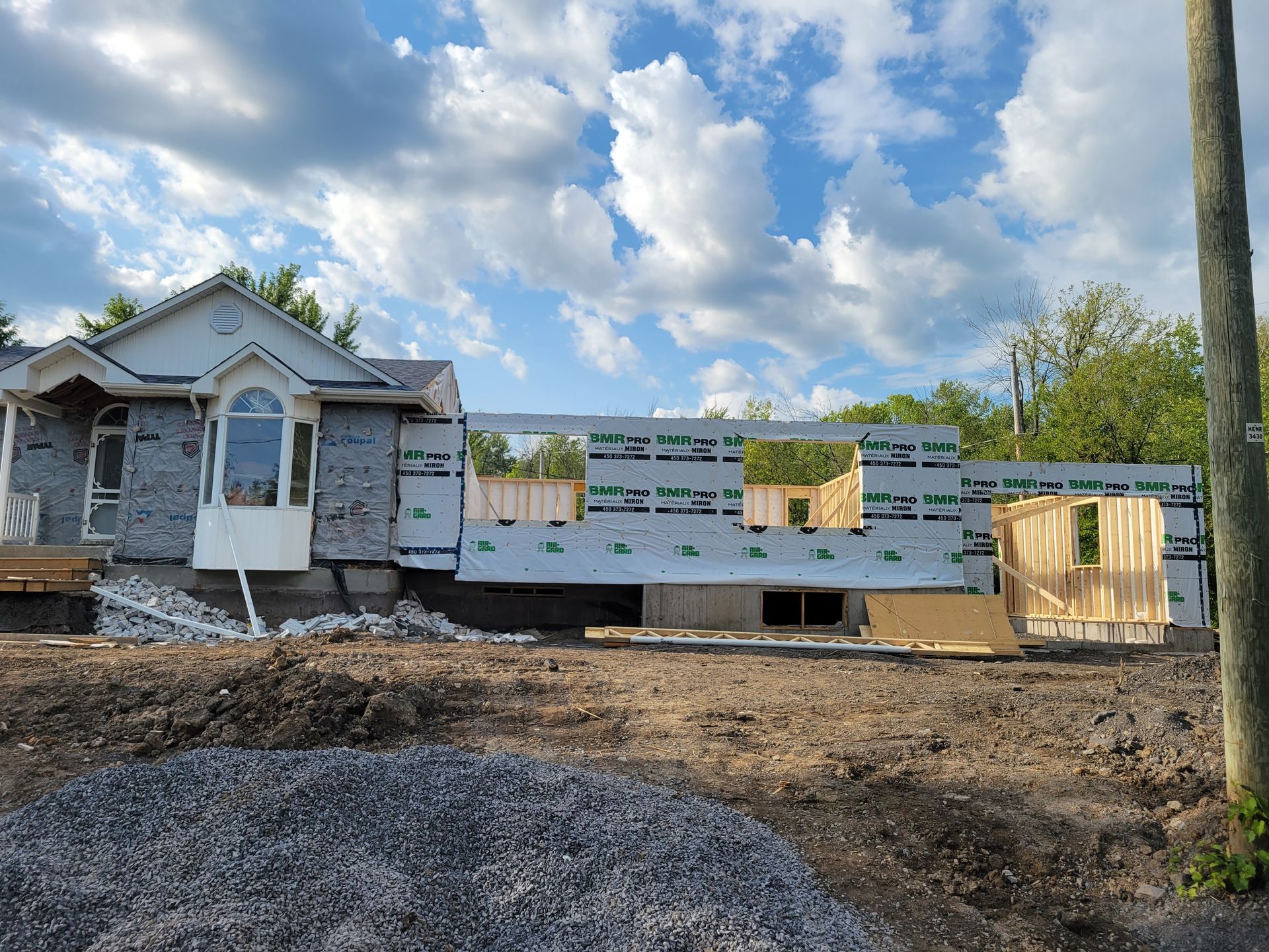 Un chantier de construction montrant une maison avec une partie déjà finie rattachée à une nouvelle extension à ossature bois.