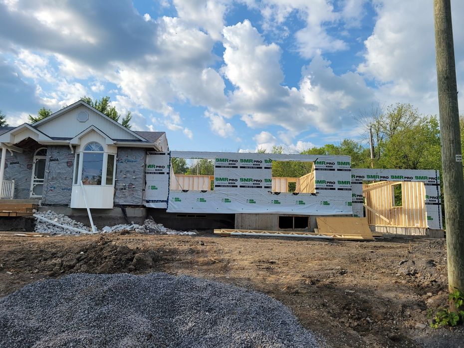 Un chantier de construction montrant une maison avec une partie déjà finie rattachée à une nouvelle extension à ossature bois.