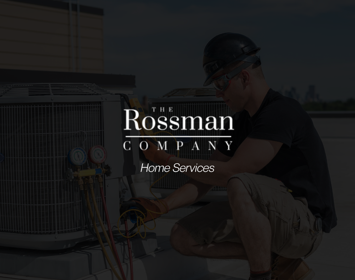A man is working on an air conditioner with a rossman company logo in the background.