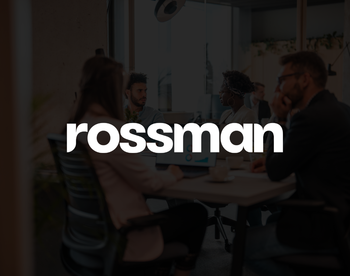 A group of people are sitting around a table with the word rossmann on it.