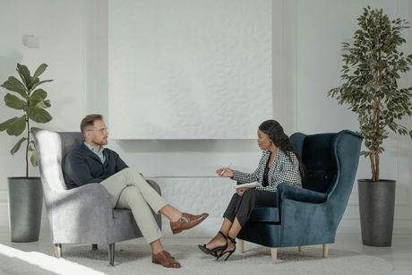 A man and a woman are sitting in chairs talking to each other.