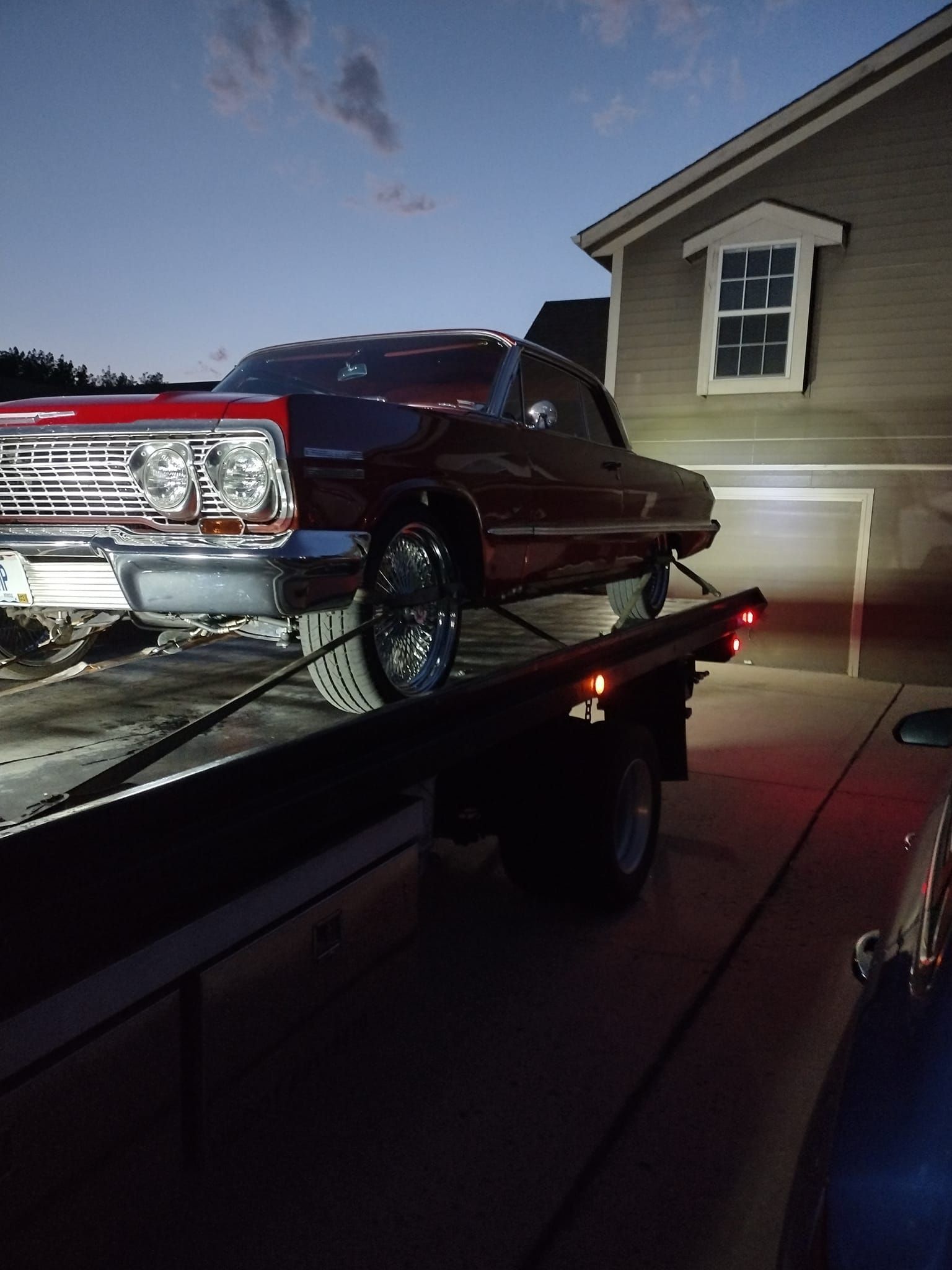 A red car is sitting on top of a tow truck in front of a house.
