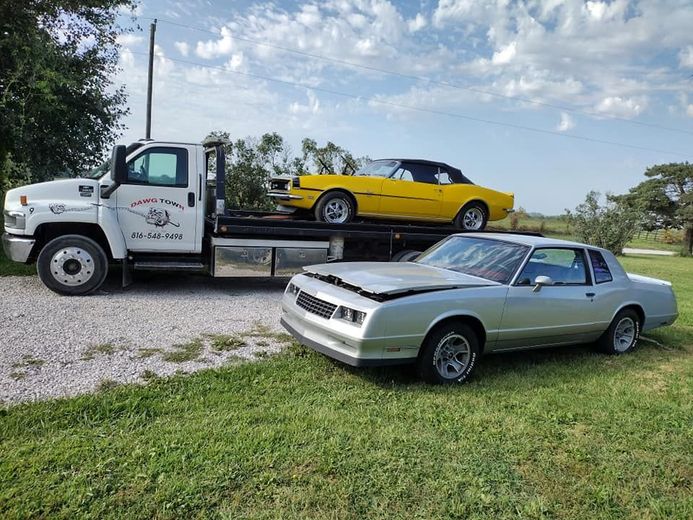 A tow truck is carrying a yellow car and a silver car.