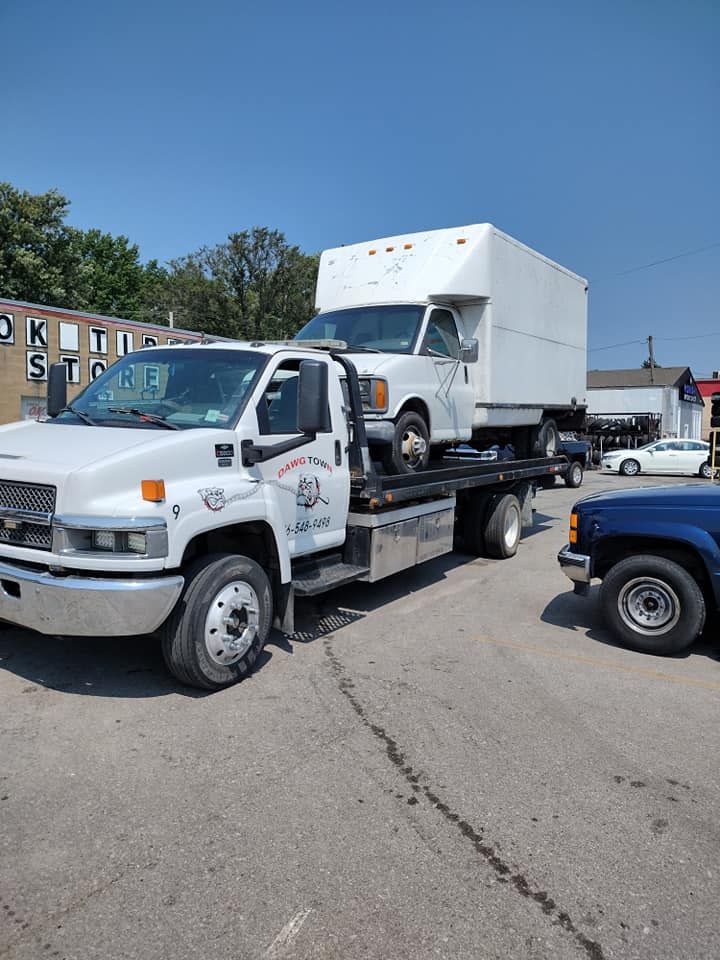 A tow truck is carrying a white van and a blue truck.