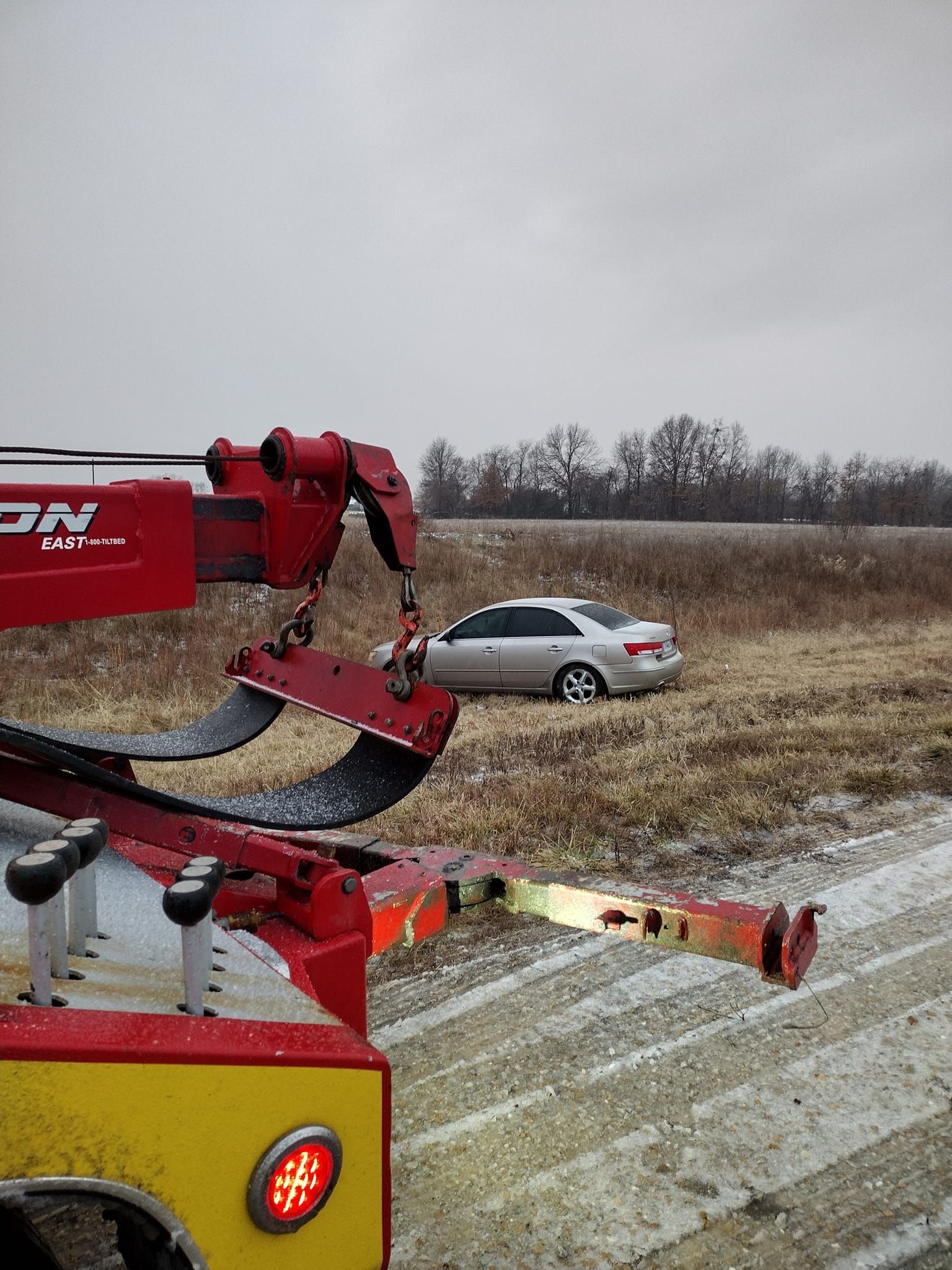 A car is being towed by a tow truck in a field.