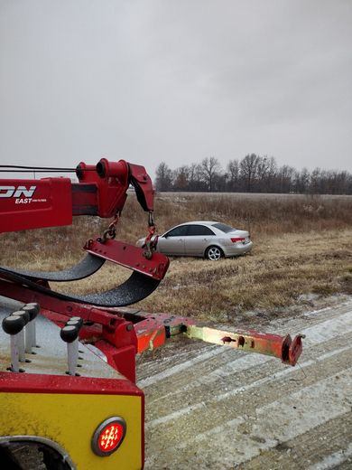 A car is being towed by a tow truck in a field.