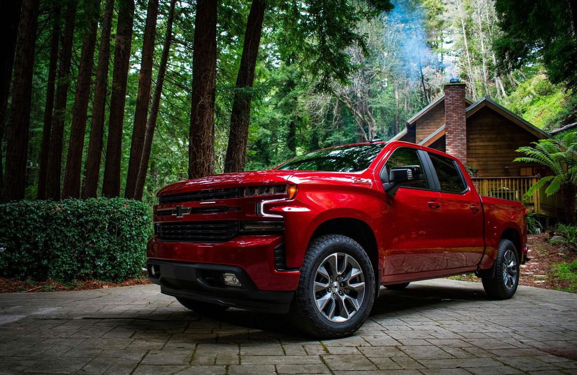 A red truck is parked in front of a house in the woods.