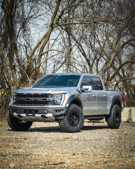 A silver ford raptor truck is parked in a gravel lot.