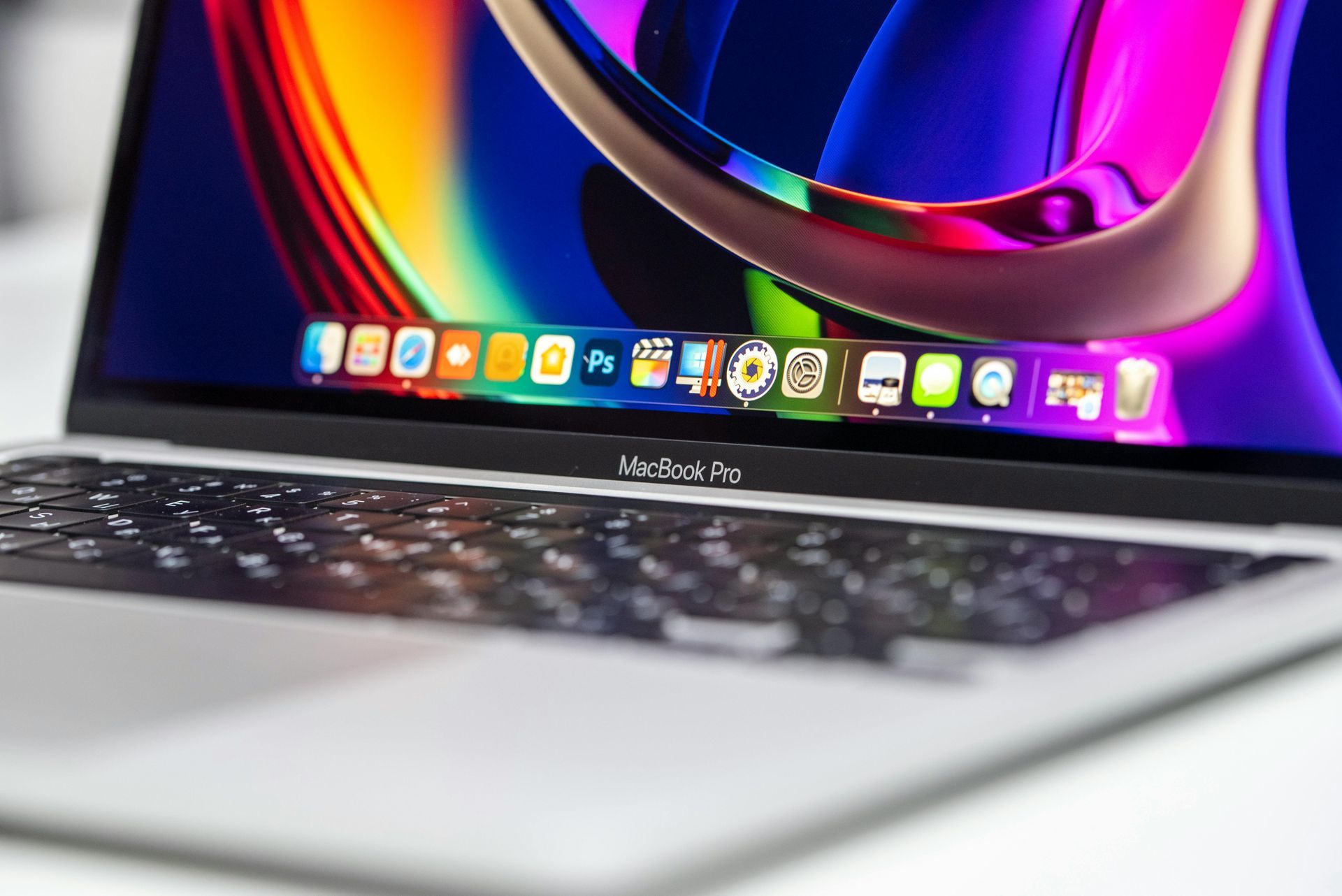 A close-up view of an open MacBook Pro showing a vibrant, colorful abstract wallpaper and an active dock of app icons.