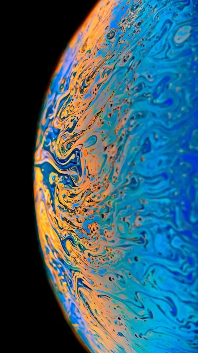 A close-up view of a curved soap film showing swirling, iridescent patterns in shades of vibrant blue and golden orange.