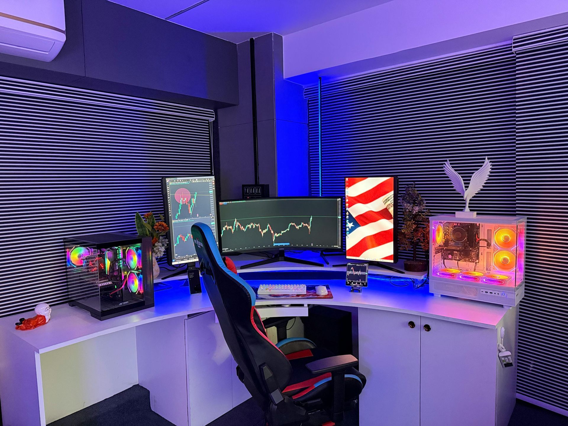 A corner desk setup with a gaming chair, multiple monitors displaying charts and a flag, and two RGB-lit computer towers.