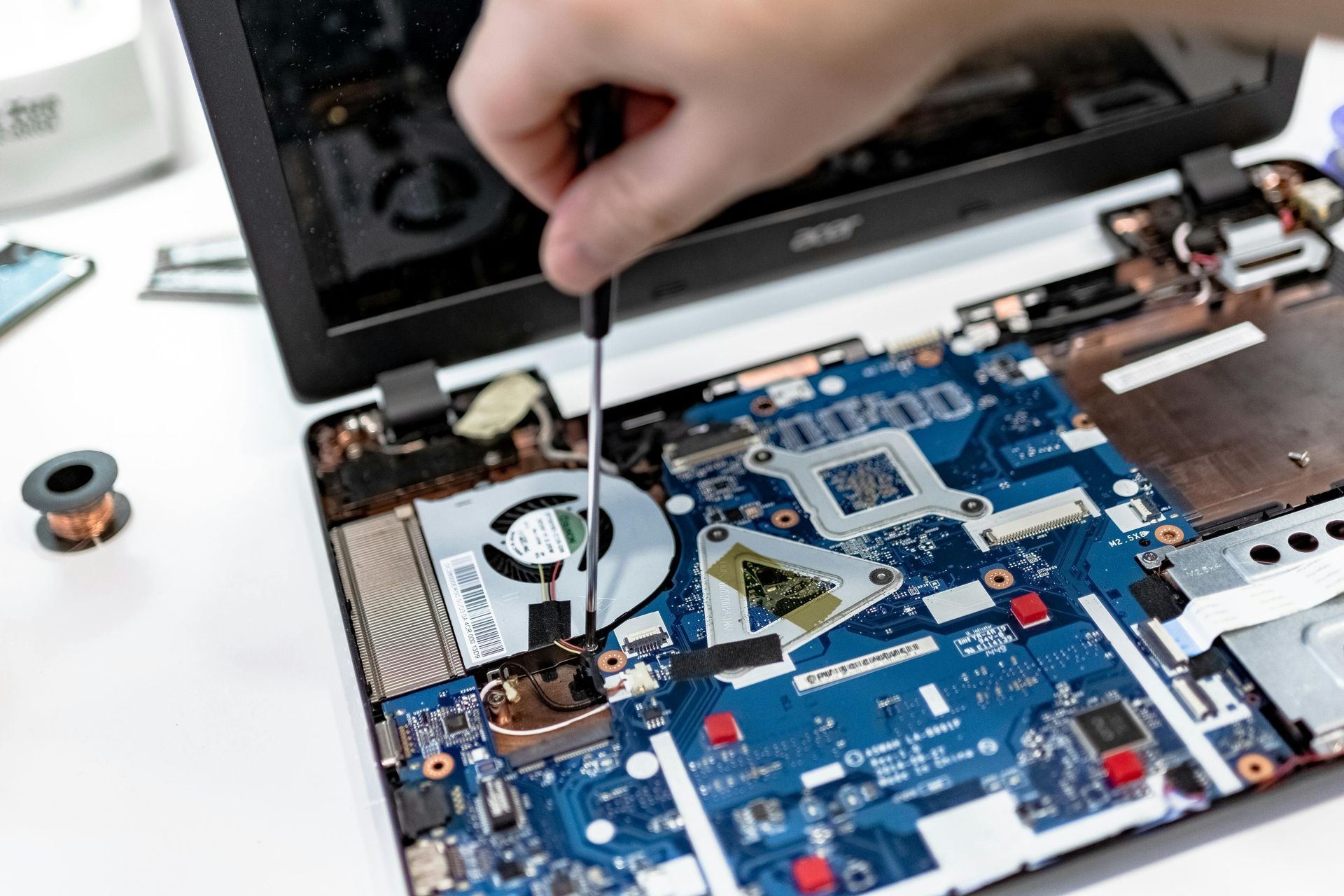 Close-up of hands using a screwdriver to repair the internal motherboard and fan components of an open laptop.
