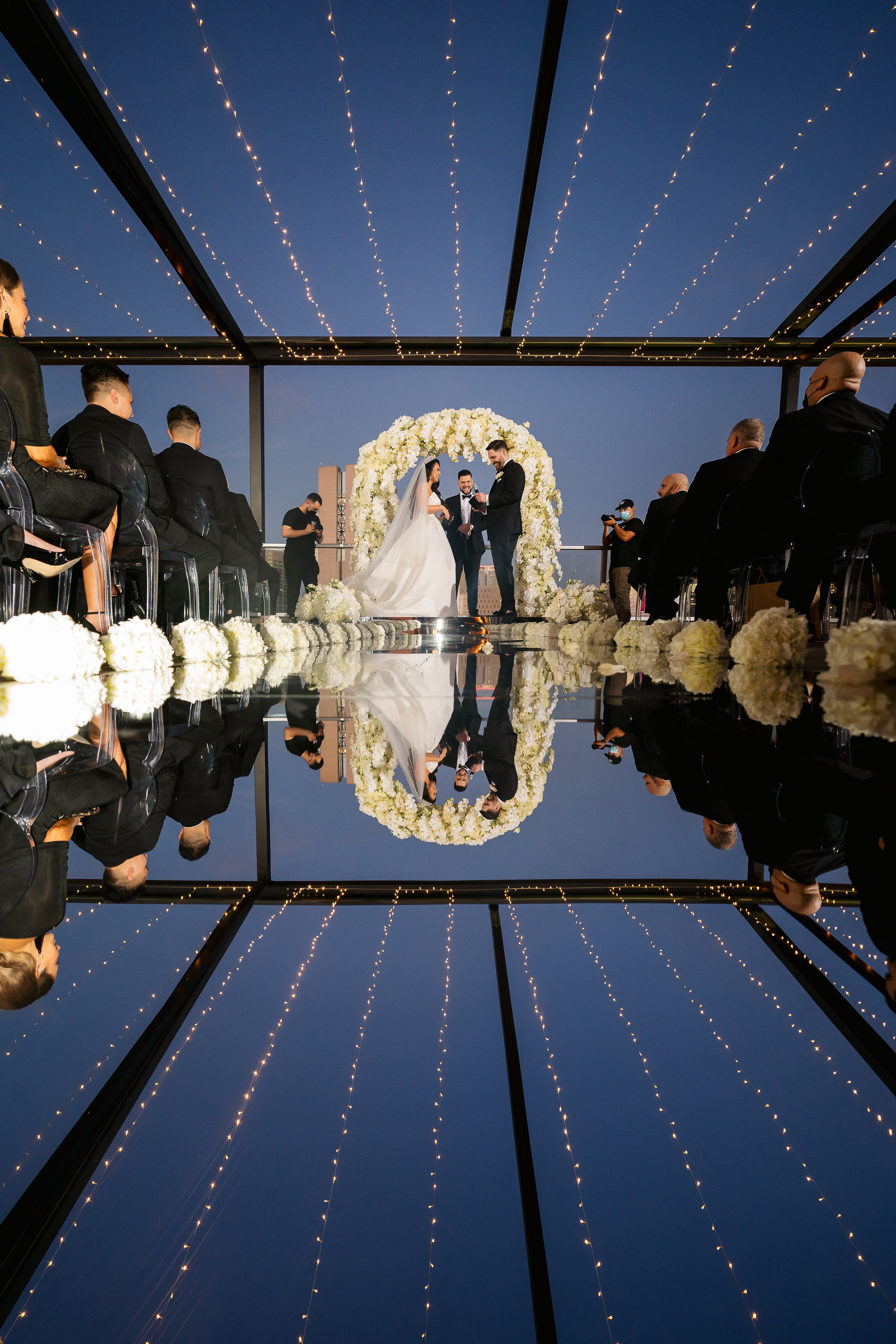 a bride and groom are getting married under a canopy and their reflection is in the water .