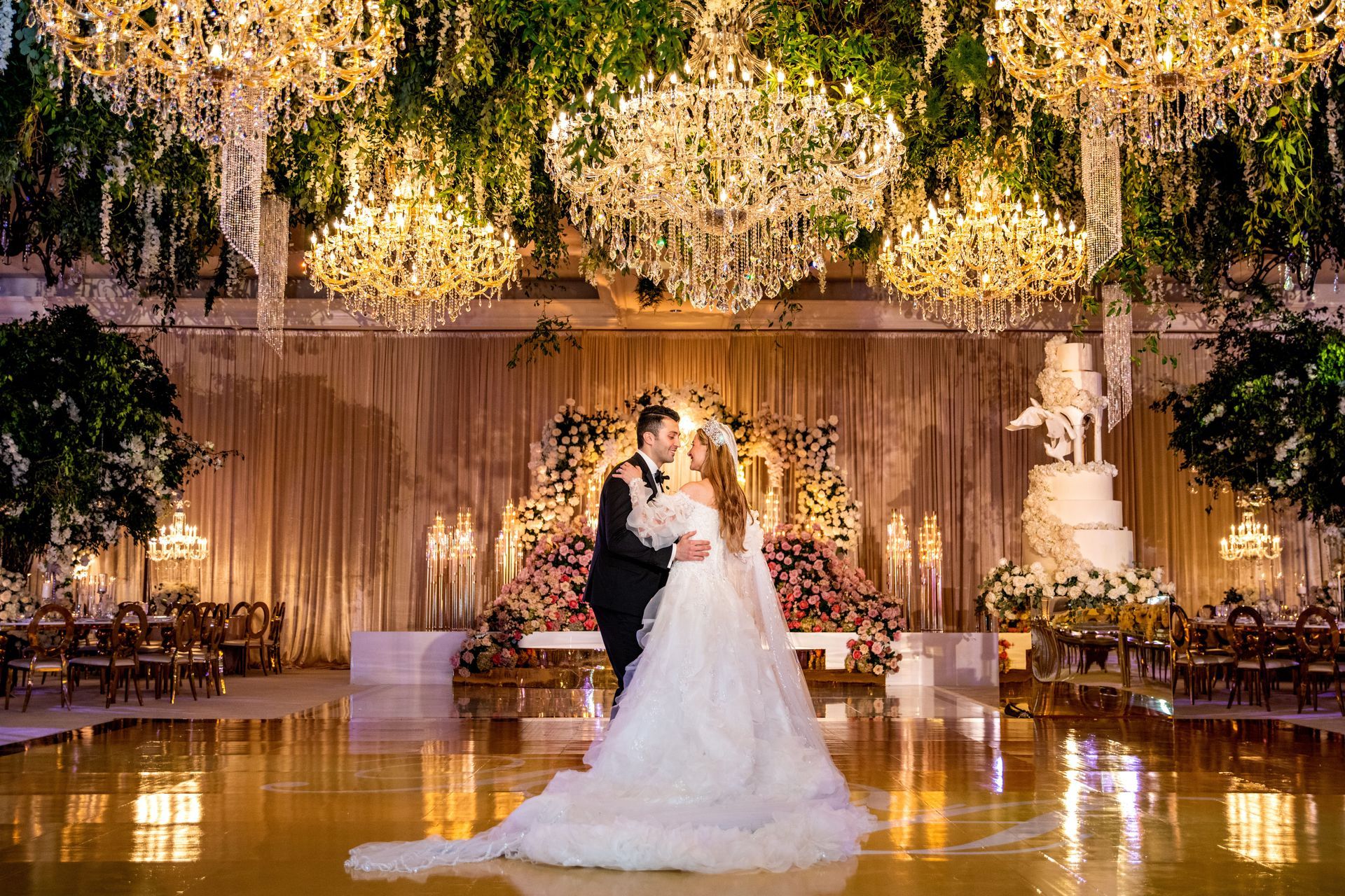 a bride and groom are dancing in front of a large chandelier at their wedding reception .
