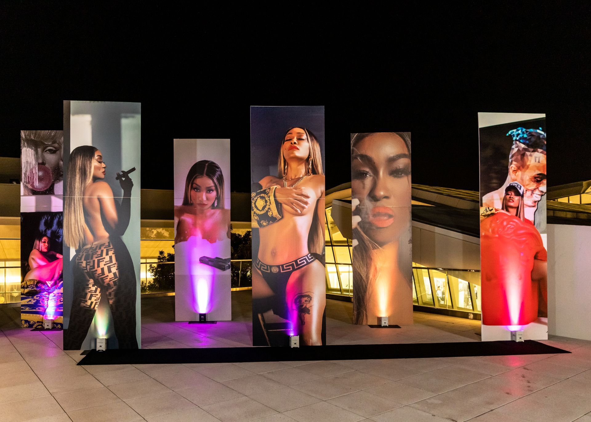 a row of pillars with pictures of women on them are lit up at night .