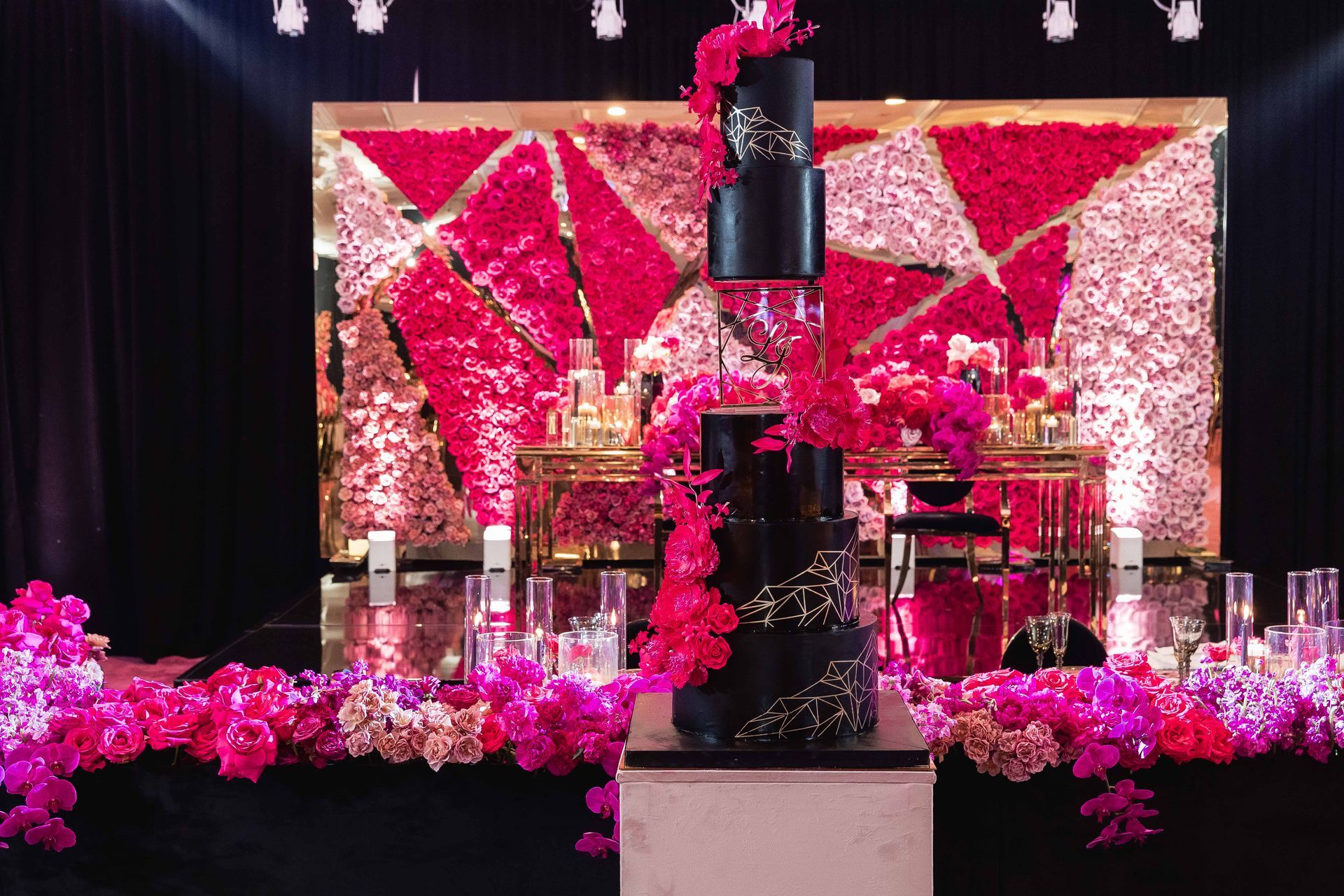 a black cake is sitting on top of a table with pink flowers .