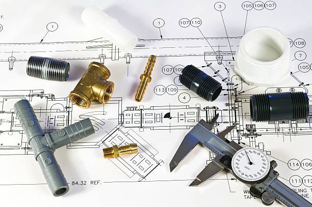 Various plumbing fittings, connectors, and a dial caliper arranged on top of a technical engineering blueprint.