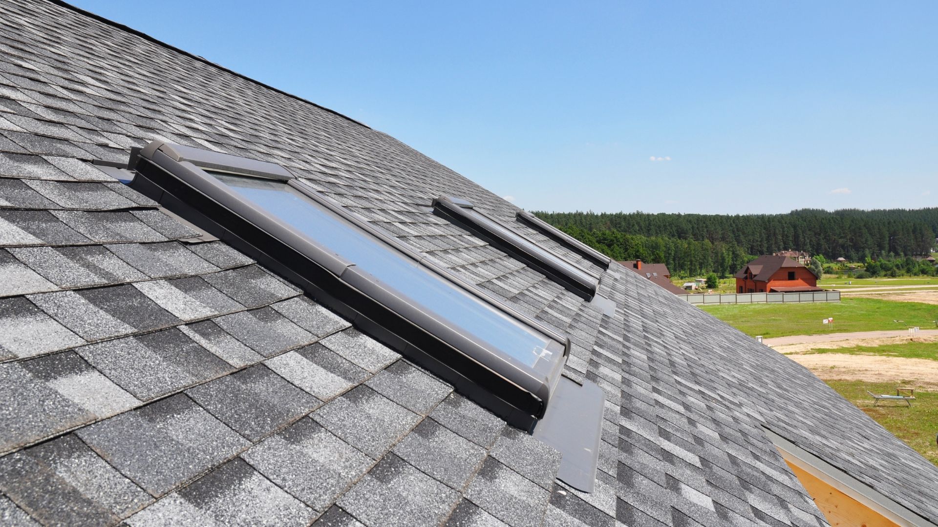 Two skylights on a gray shingled roof under a clear blue sky.