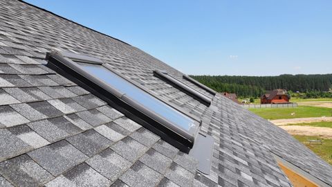 Two skylights on a gray shingled roof under a clear blue sky.