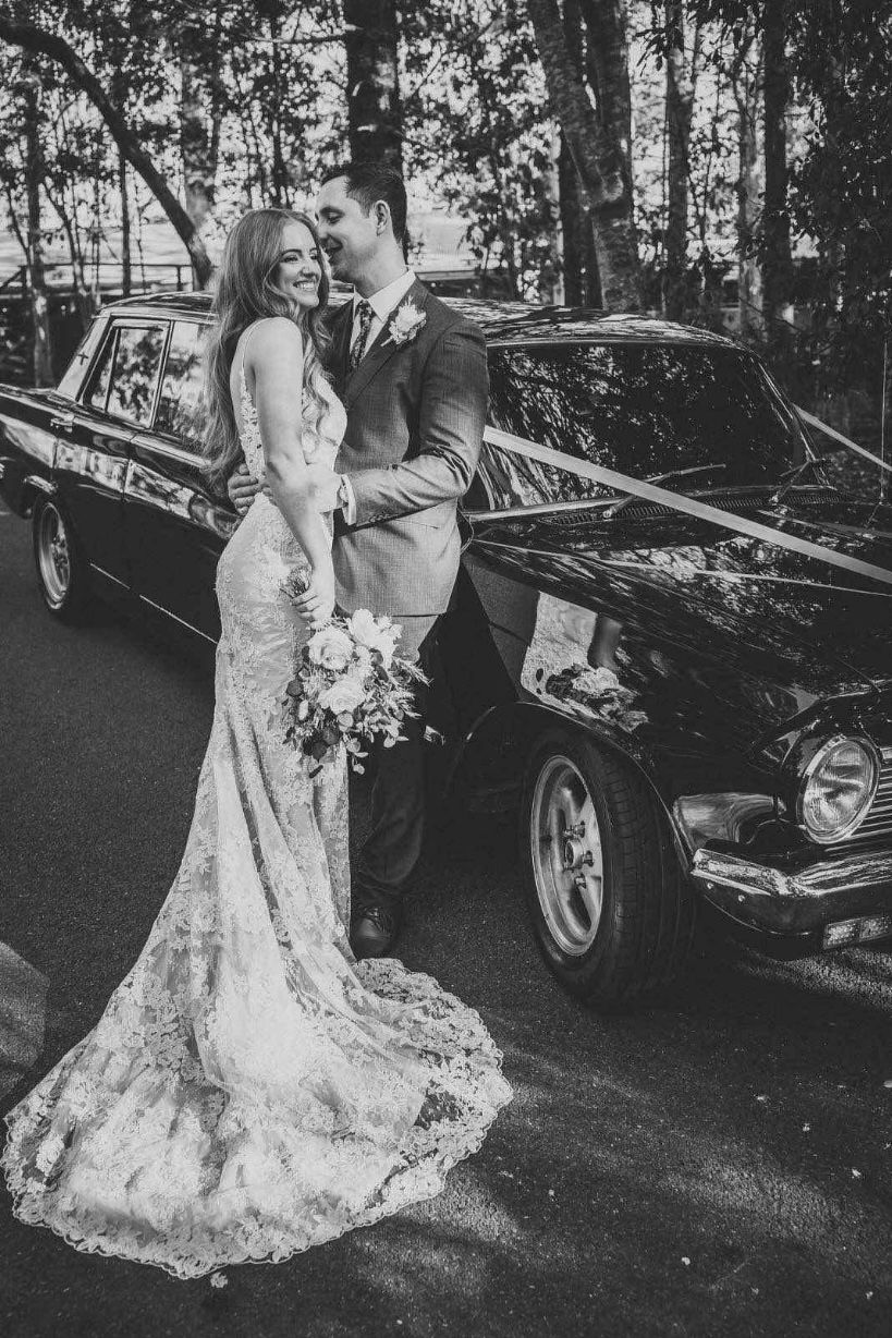 A Bride And Groom Are Walking Down A Street Next To A Car — Noosa Premier Stretch Holden Transfers In Sunrise Beach, QLD